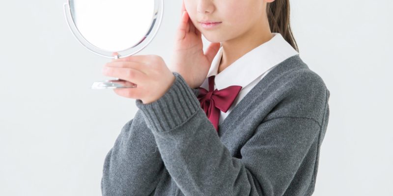 鏡を見て肌に手を触れる女の子