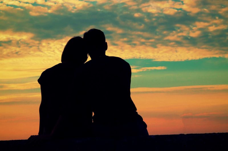 寄り添っているカップルのシルエットと夕日