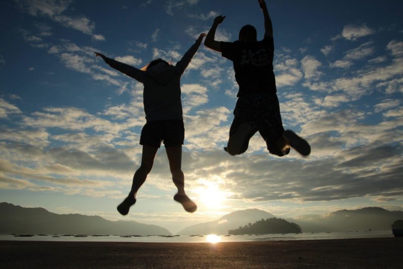 朝日に向かってジャンプをしている人
