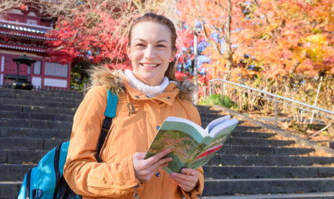 紅葉のお寺を散策している女性が次はどこ行こうかと計画を練っているとこ