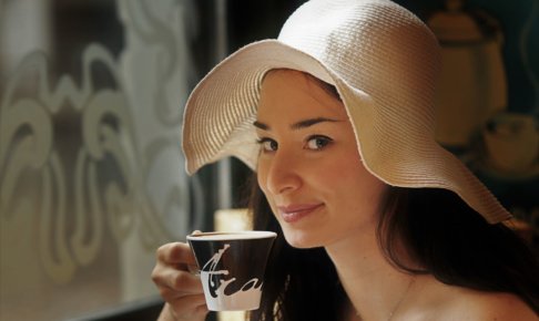 帽子を被ってカップで飲み物を飲む女性