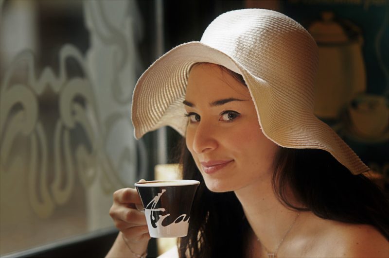 帽子を被ってカップで飲み物を飲む女性