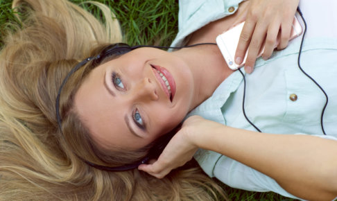 芝生に寝ころびながらスマートフォンで音楽を聞く外国人女性