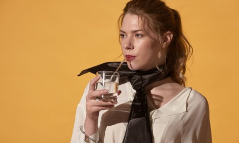 コップの水をストローで飲む白い服を着用した外国人女性