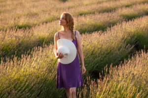 ラベンダー畑にいる紫の服を着用した帽子を持っている外国人女性