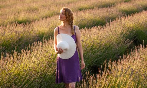 ラベンダー畑にいる紫の服を着用した帽子を持っている外国人女性