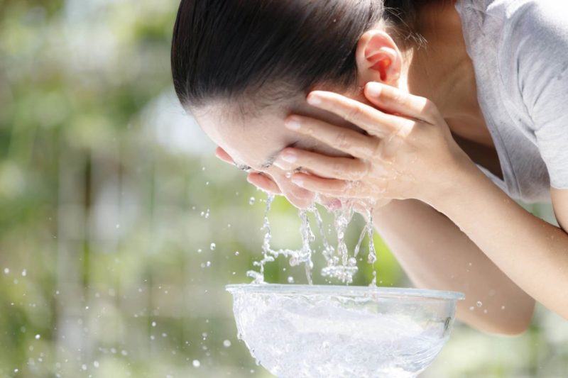 緑の背景で顔をパシャパシャ洗っている日本人女性