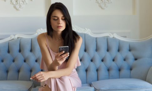 ソファーに座ってスマートフォンを操作している外国人女性