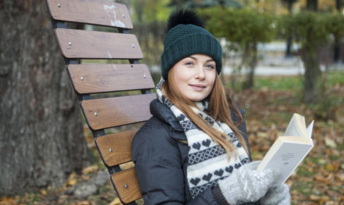 木製のイスで読書している冬装備の女性