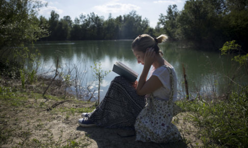 水辺のそばで座って本を読んでいる外国人女性