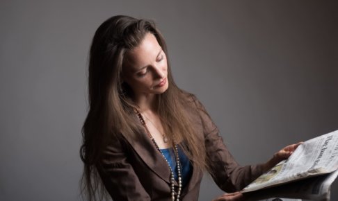 黒い背景の中新聞を読んでいる女性