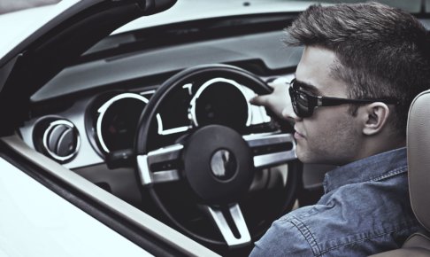 車の運転席に座ってステアリングを握っているサングラスを掛けた外国人男性