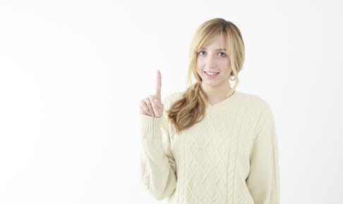 指を指している白いニットの女性