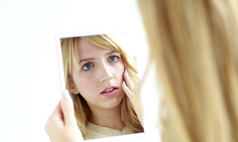 鏡をのぞいて悩む金髪の女性