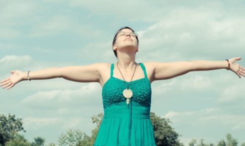 青空の下でワンピースの女性が手を広げているところ