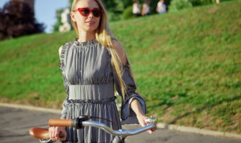 自転車を支えているサングラスをしたノースリーブのワンピースを着用した外国人女性