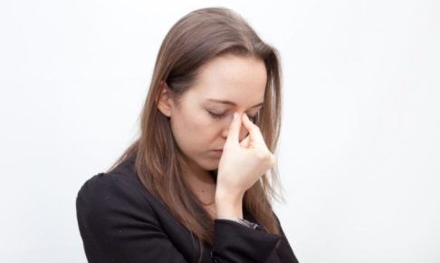 目が疲れて目頭を押さえている黒いスーツ着ている女性