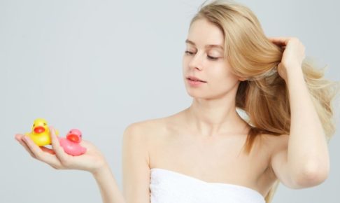 アヒルのおもちゃを２つ手に取り、髪をなびかせているバスタオルの女性