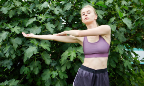 大きな葉っぱの茂みの前でストレッチをしている女性