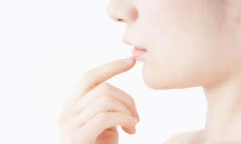 色白の横顔の女性が下唇の少し下辺りを人差し指で触れている。画像はデコルテ付近から上で肌に身に着けているものはない。