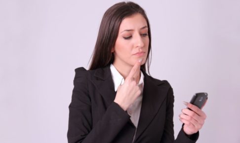 スマホを見ながら顎に指を添えてお悩み中の白人女性