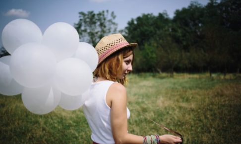 晴れた草むらの中で麦わら帽子の女の子が白い風船を持っている