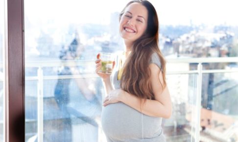 日の当たるベランダで水を持って微笑んでいる妊婦