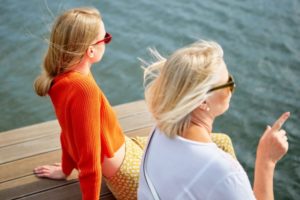 海沿いに座り景色を眺めている女性二人の後頭部