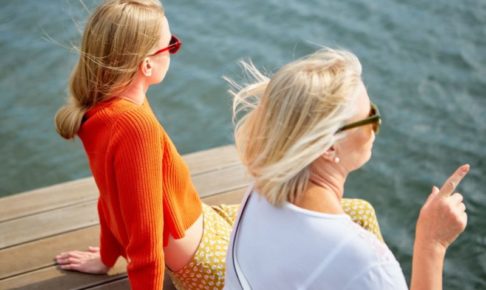 海沿いに座り景色を眺めている女性二人の後頭部