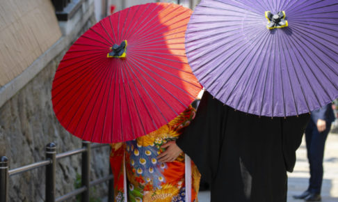 和装をしてピンクと紫の番傘を差したカップルの後ろ