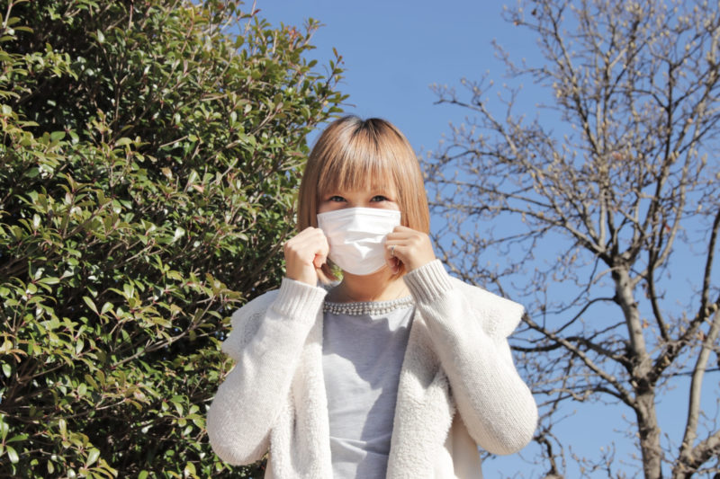 青い冬空の中、マスクで顔を隠している女性