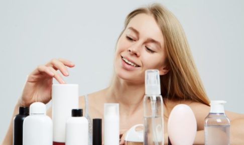 何本も並ぶ化粧品を選ぶブロンド長髪の白人女性