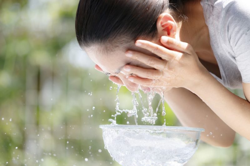 透明なボールに入れた水で洗顔中の女性