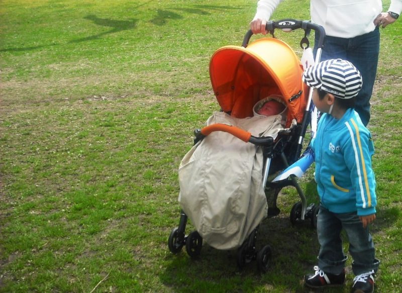 芝生の中お散歩に着ている新生児とそのお兄ちゃん