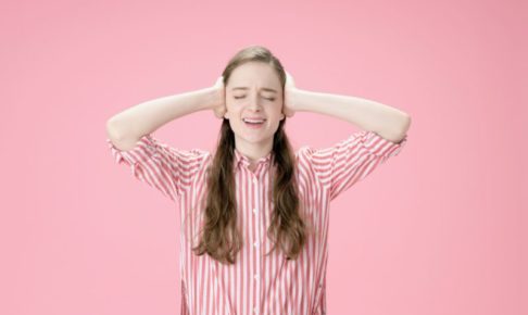 頭を抱えて声を上げるピンクストライプシャツの白人女性