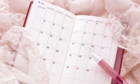 ピンクのレースに囲まれた手帳とピンクのボールペン