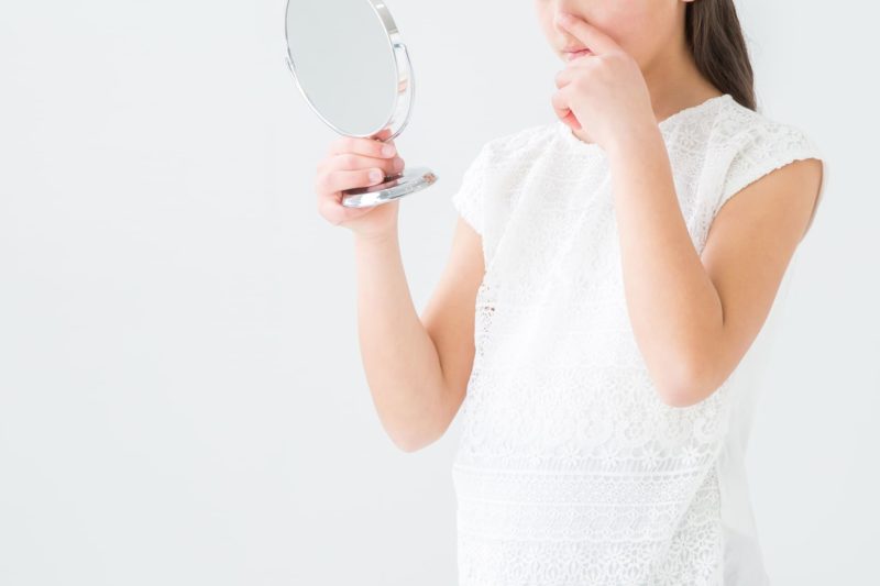 手に持った鏡で顔をみる小学生
