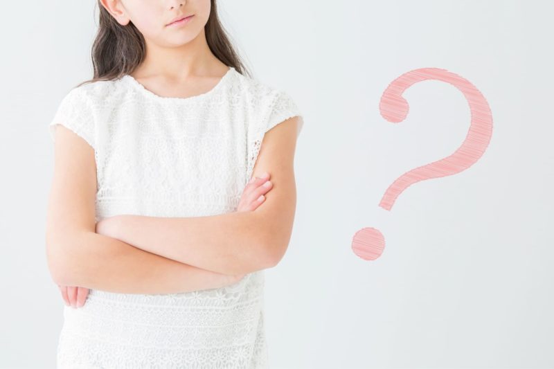 腕を組み考える女の子とピンクのはてなマーク