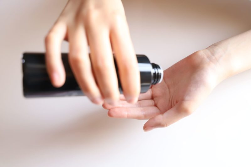 黒い化粧水の瓶を傾ける手