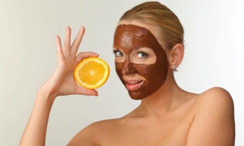 茶色い泥パックをしてオレンジを持ちながらポーズしている女性