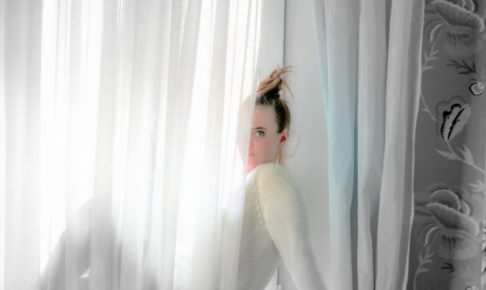 白いカーテンから半分顔をのぞかせている外国人女性