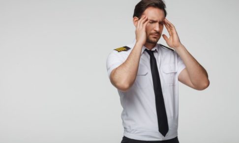 眉間にしわを寄せて頭を抱えている男性パイロット