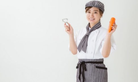 ニンジンとピーラーを持ってるカフェ勤務風の女性