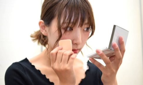 手鏡を見ながら真剣に化粧下地を塗る女性