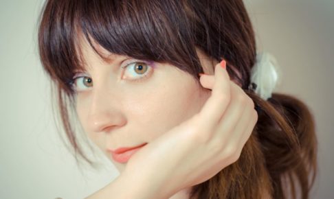 髪を一つに結んでコーラルのネイルを付けている女性の45度のアップ