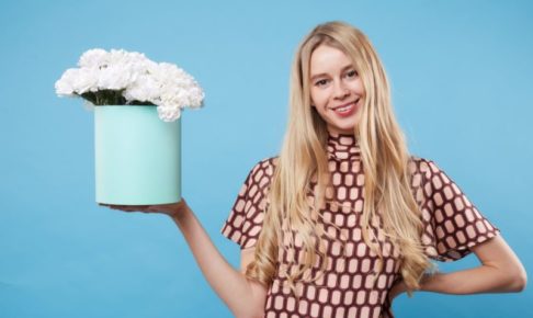 水色の背景で白いカーネーションを持ちながらにこやかにしている女の子