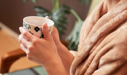 暖かそうなガウンを着て温かい飲み物を持っている手元