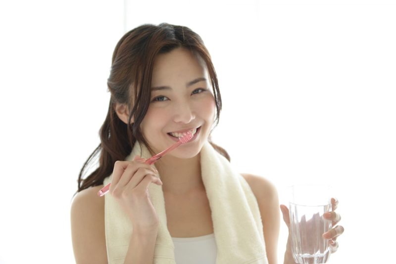 爽やかな笑顔の女性が起床後と思われる光景のなかで歯を磨いている