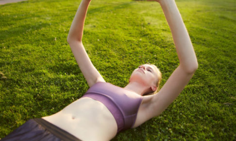 芝生に仰向けになって一生懸命ストレッチをしている女性