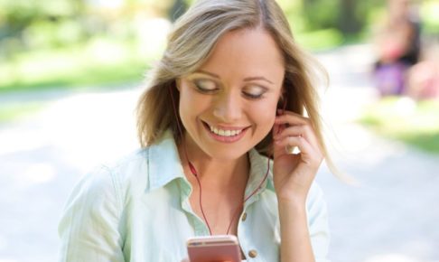 夏の公園でスマホで音楽を聴いて楽しんでいる女性